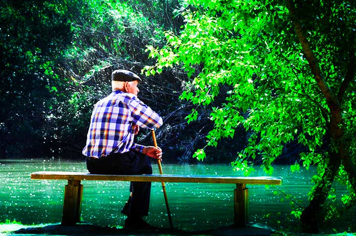 Anciano sentado en banco frente a un río