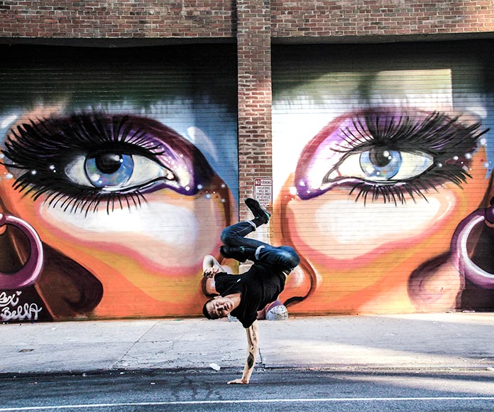 Bailarín de hip hop frente a mural de ojos de mujer pintado en la pared