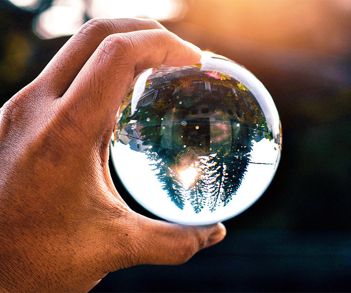 mano sujetando bola de cristal en la que se refelja el paisaje al revés