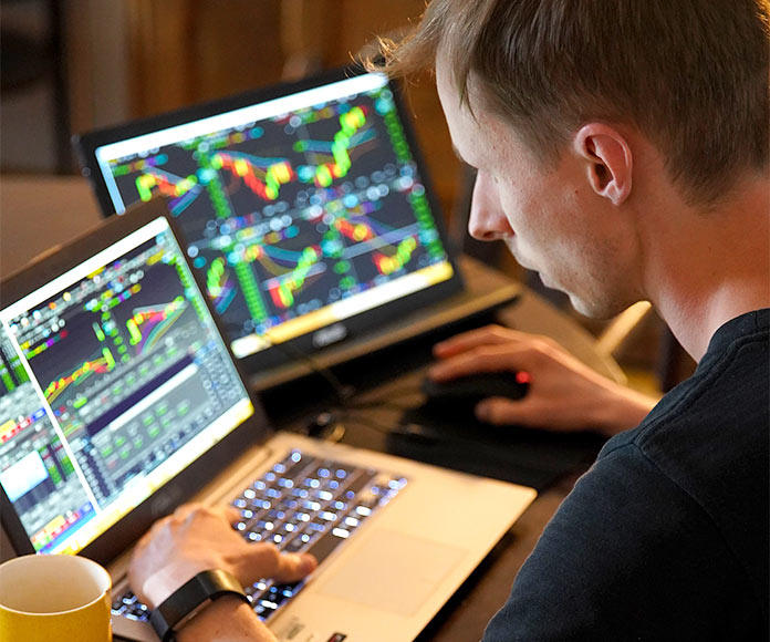 Hombre broker frente a dos ordenadores portátiles con gráficas de divisas o criptomonedas