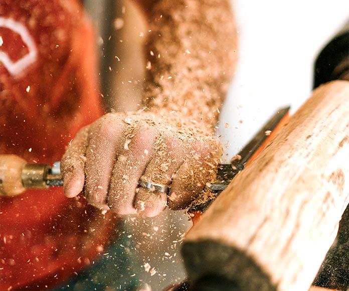 Detalle de mano de carpintero trabajando con una madera en un torno.