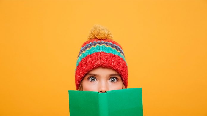 chica con gorro de invierno detrás de un libro