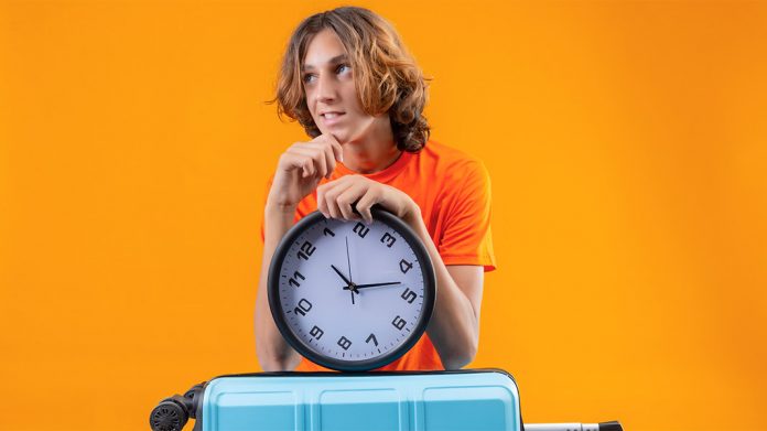 chico esperando con una maleta de viaje y un reloj de pared