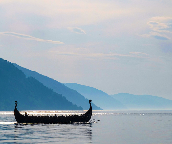 Barco vikingo navegando en un paisaje con montañas al fondo