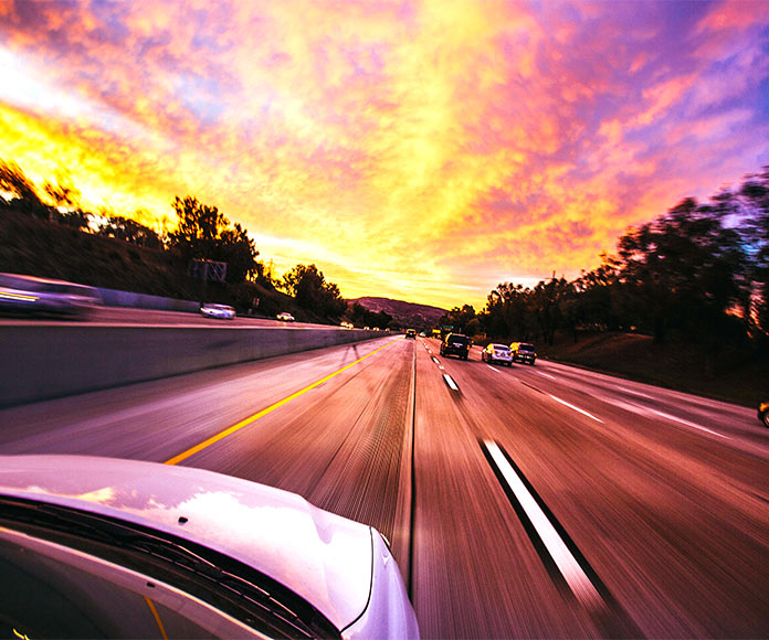 Coches transitando por autopista hacia la puesta de sol