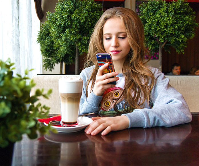 Chica sentada en cafetería mirando el móvil