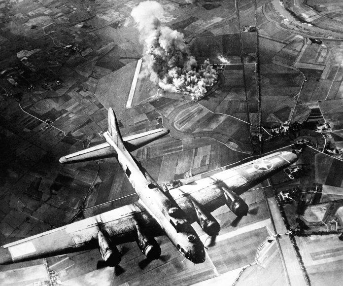 Avión militar en primer plano en medio de un bombardeo
