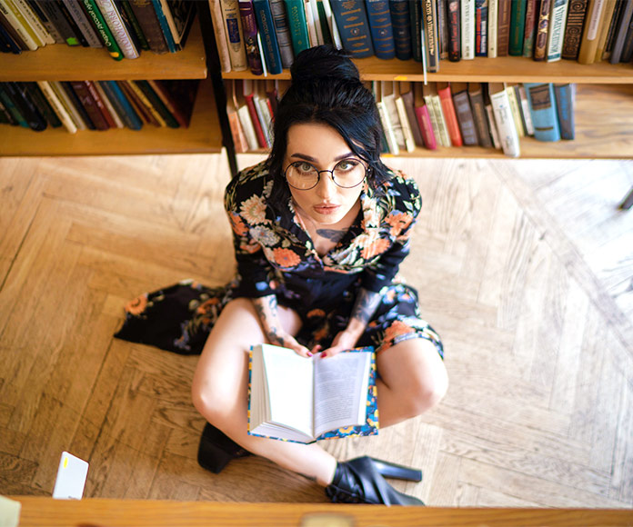 Mujer joven sentada en el suelo de una biblioteca con un libro