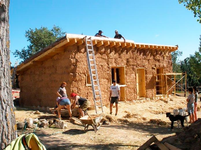 Grupo de personas construyendo una casa con fardos de paja