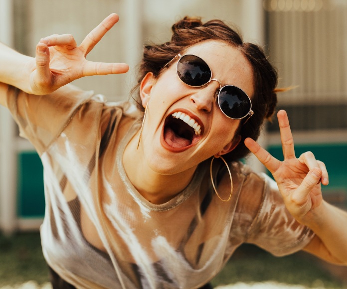 Chica sonriendo a la cámara haciendo gestos con las manos.