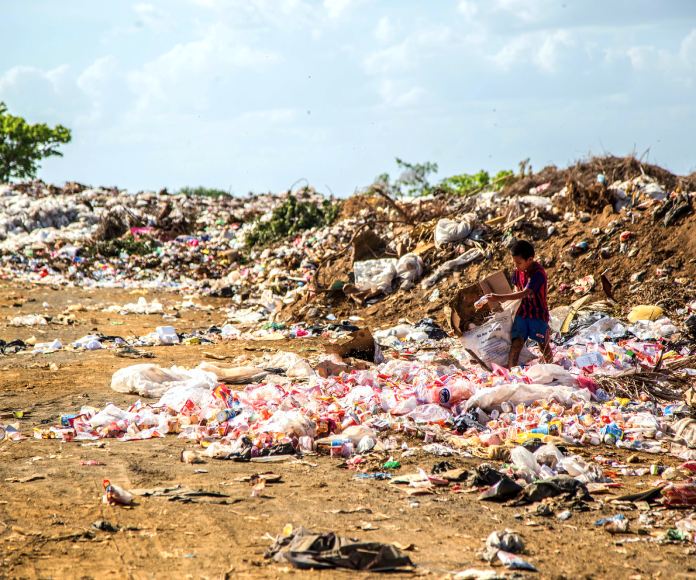 Niño caminando entre montones de basura.