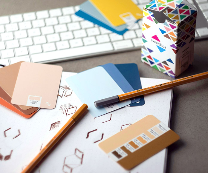 Escritorio con elementos de diseño gráfico: logotipos, colores, lápices, caja de producto.