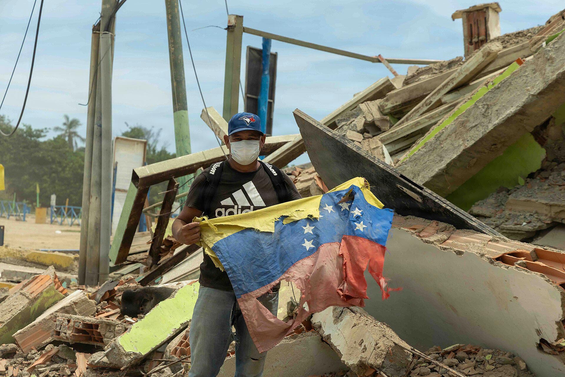 Un venezolano sostiene una bandera nacional junto a su restaurante completamente destruido