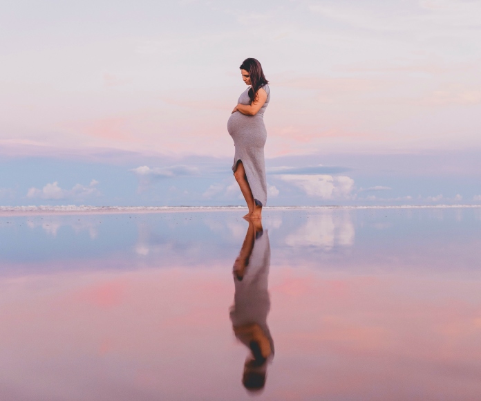 Mujer embarazada reflejada sobre un cuerpo de agua.