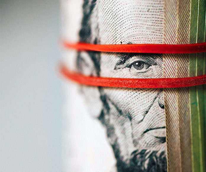 Primer plano de billete de dólar enrollado con gomas rojas sobre la cara de Lincoln