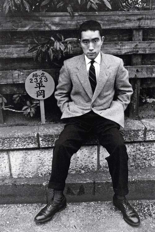 Foto en blanco y negro de Mishima sentado en el frente de una casa. 