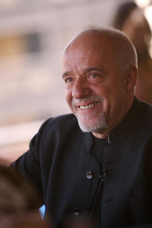 Paulo Coelho vestido de negro sonriendo hacia la izquierda. 