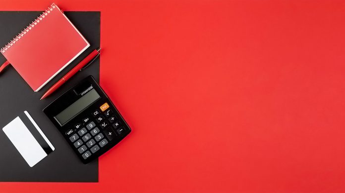 calculadora, tarjeta de crédito y libreta sobre escritorio rojo