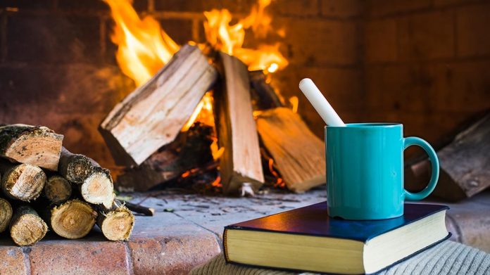 libro y taza de desayuno junto a chimenea encendida