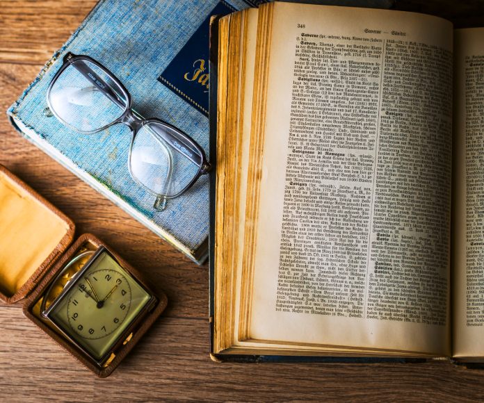 Mesa con dos libros, un par de lentes y un reloj antiguo.