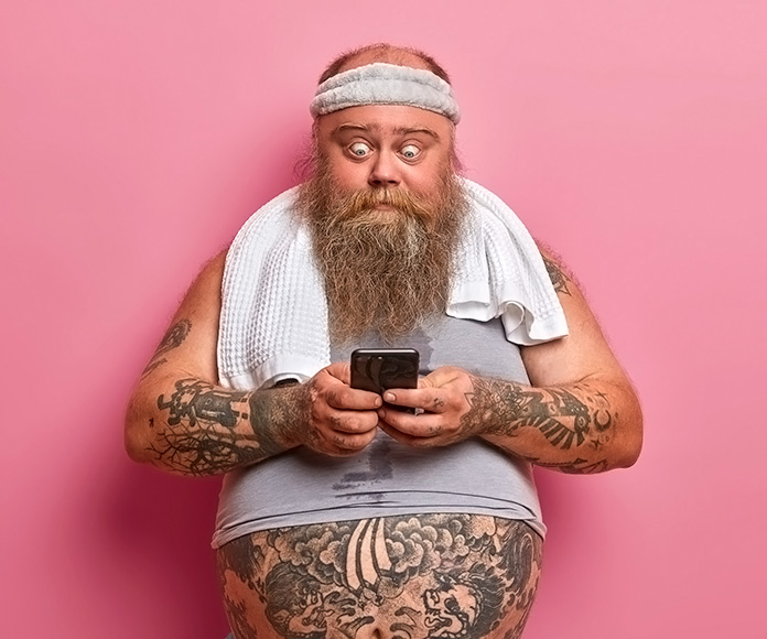 hombre tatuado y con barba sorprendido mirando su smartphone