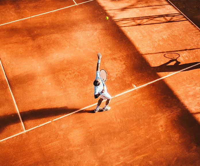 Jugador de tenis haciendo un saque en una pista de tenis de tierra batida