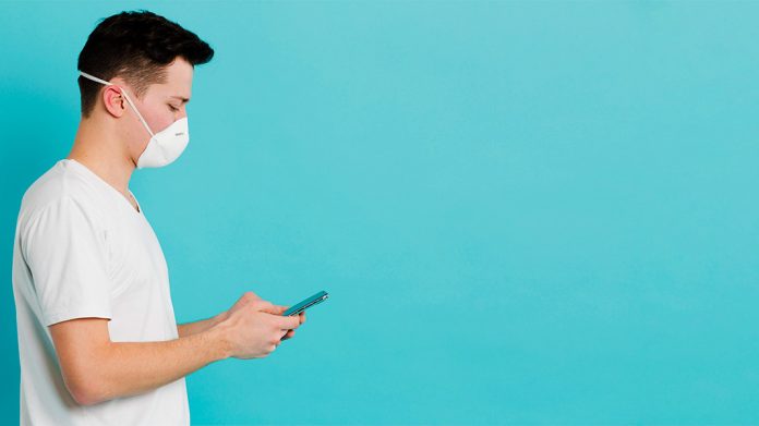 joven con mascarilla sujetando un teléfono móvil