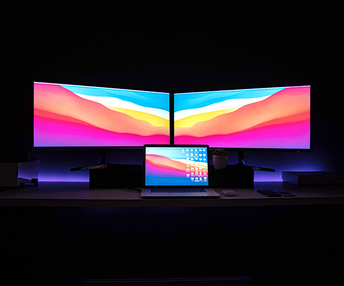 Dos monitores y un portátil con fondos coloridos