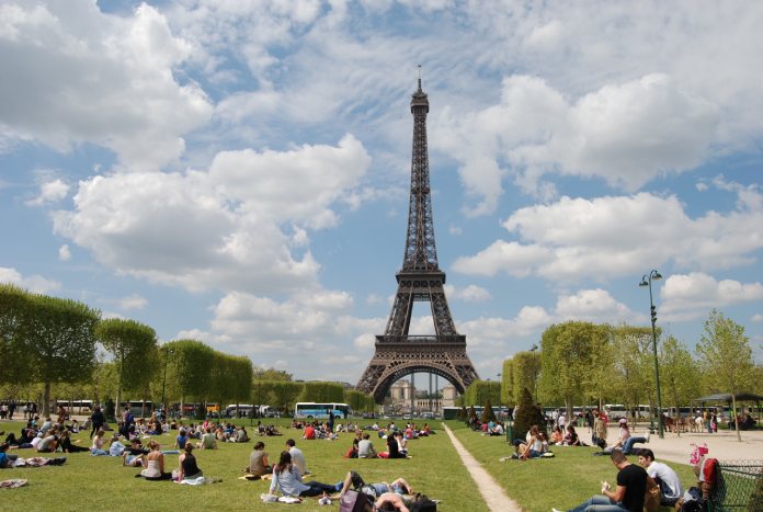 La imagen muestra a varias personas tomando el sol en los jardines de la Torre Eiffel. 