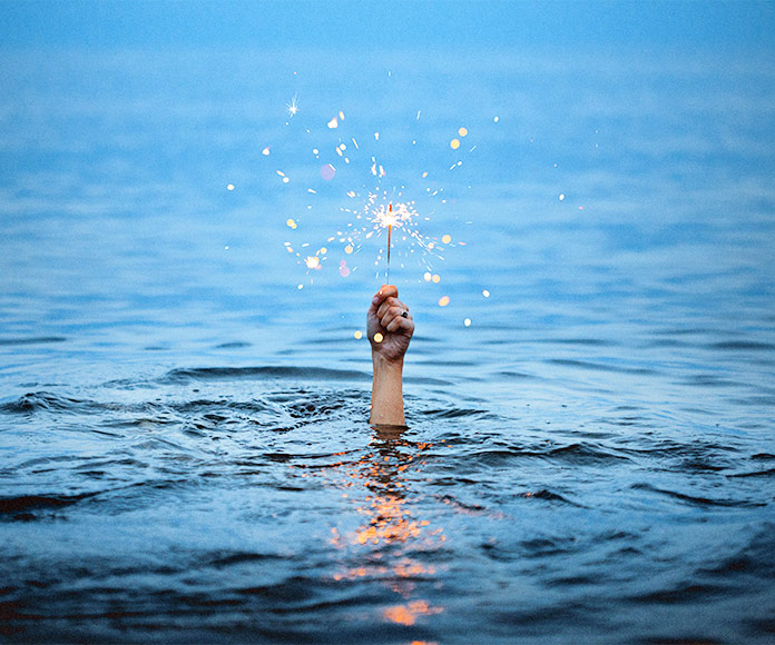 Mano saliendo del mar con una bengala encendida