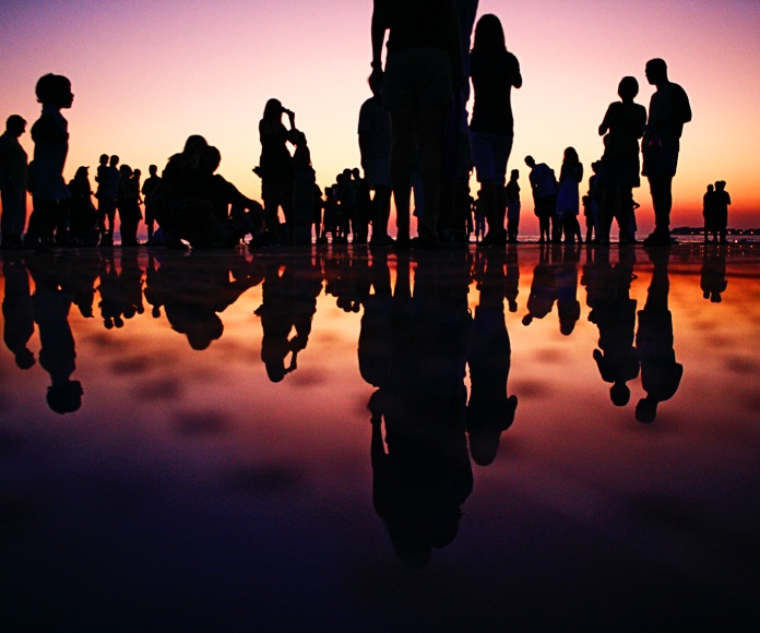 Siluetas de varios grupos de personas frente a un atardecer.