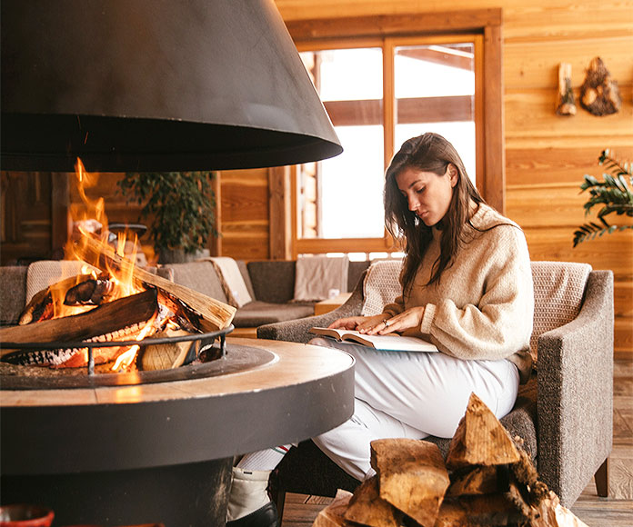 Mujer sentada leyendo frente a una chimenea en invierno