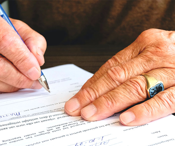 Detalle de las manos de un hombre mayor firmando un documento