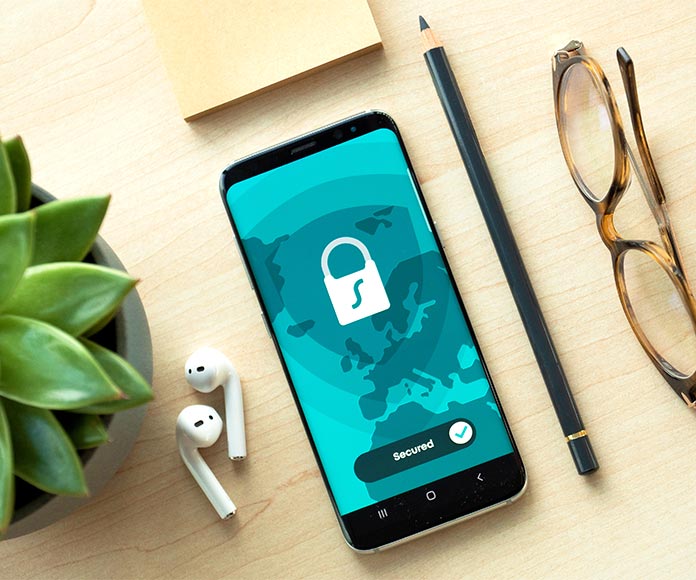 Teléfono móvil con pantalla de seguridad sobre una mesa con planta y gafas de ver.