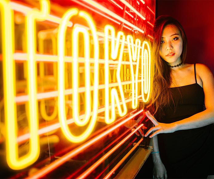 Mujer asiática apoyada en un rótulo luminoso de Tokio