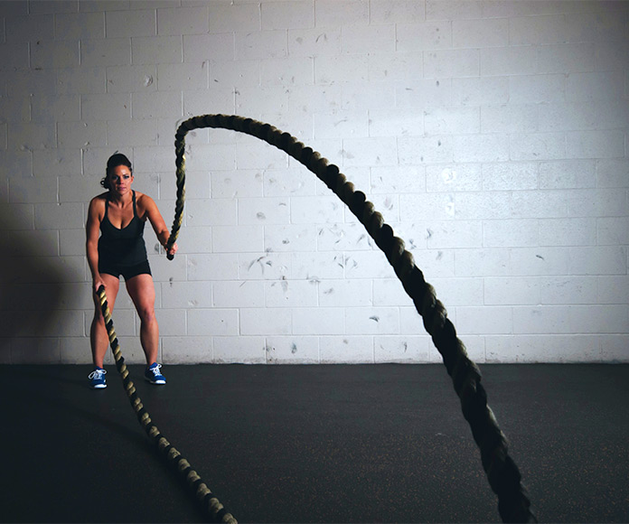 Mujer entrenando a crossfit con cuerdas en un gimnasio