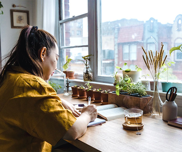 Mujer escribiendo en una libreta frente a ventana