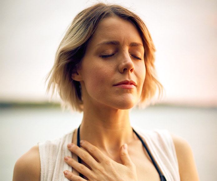 Mujer meditando con los ojos cerrados y la mano en el pecho.