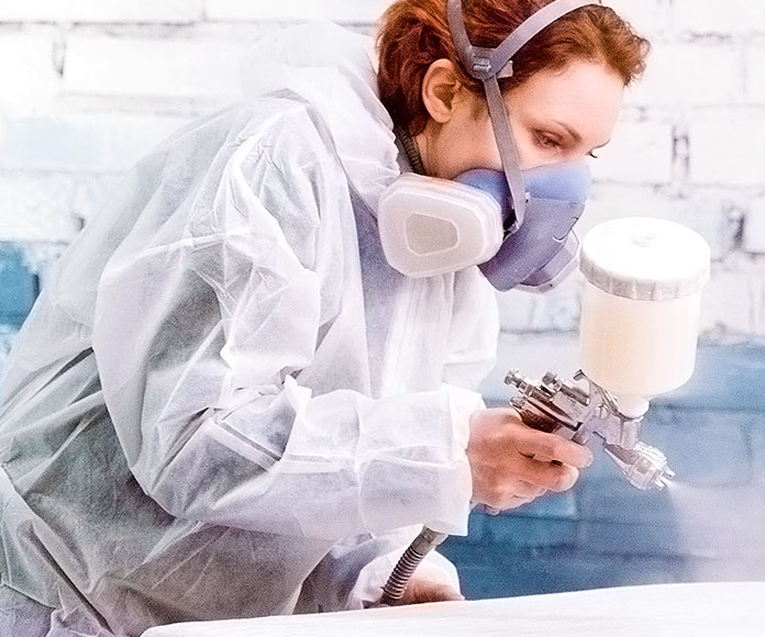 Mujer pintando o lacando un mueble con spray blanco y mascarilla