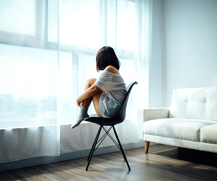 mujer en soledad con depresión sentada frente a ventana