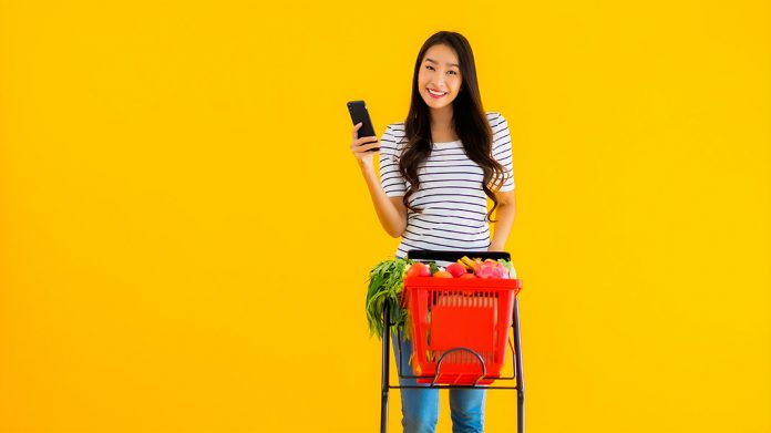 chica llevando un carrito de supermercado lleno de comida con un móvil en la mano