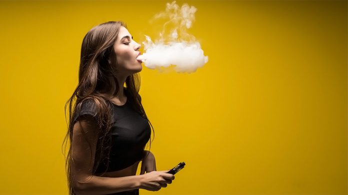 mujer vapeando delante de una pared amarilla