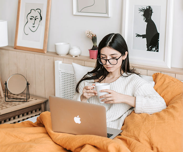 Mujer mirando un ordenador portátil en la cama con una taza de café