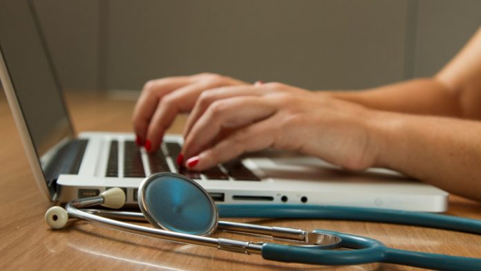 Persona trabajando en una computadora portátil y un estetoscopio verde cerca