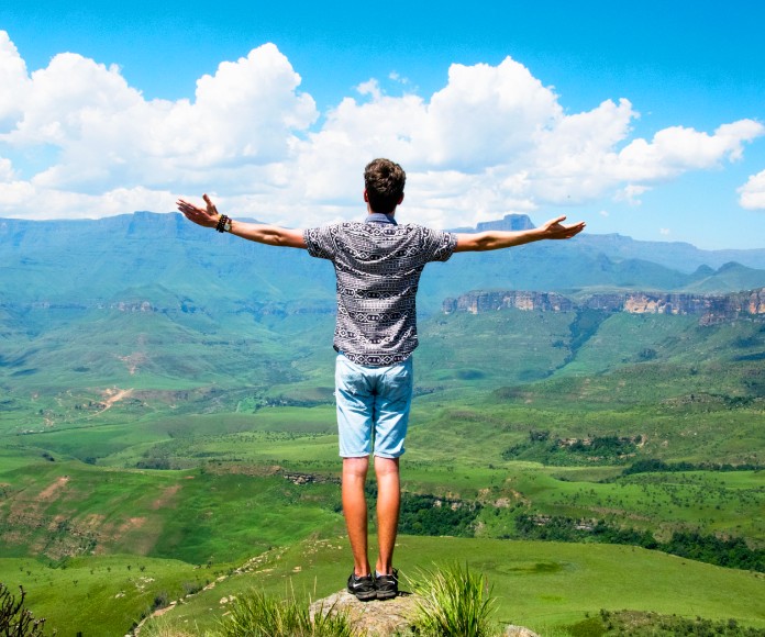 Hombre blanco con sus brazos abiertos frente a un paisaje abierto.