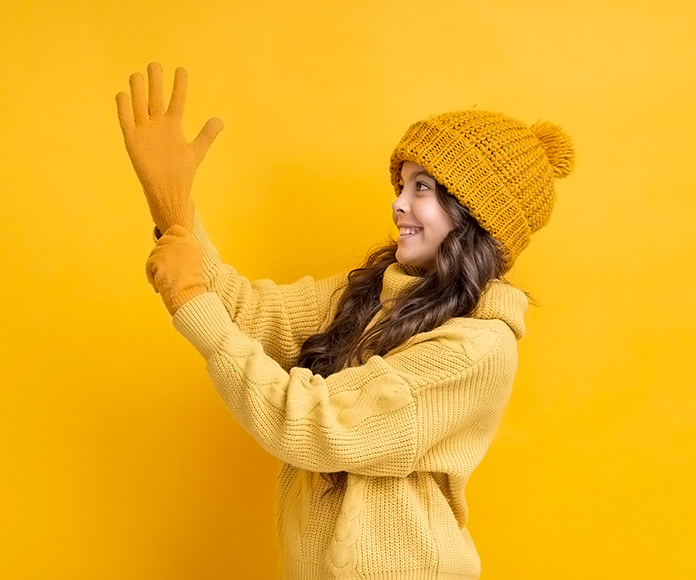 niña vestida con abrigo y gorro de invierno poniéndose unos guantes