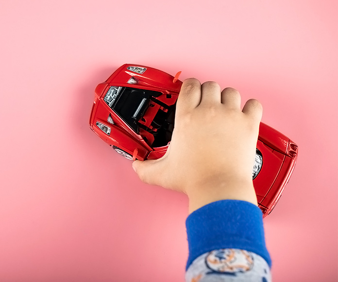 mano de niño jugando con un coche rojo de juguete