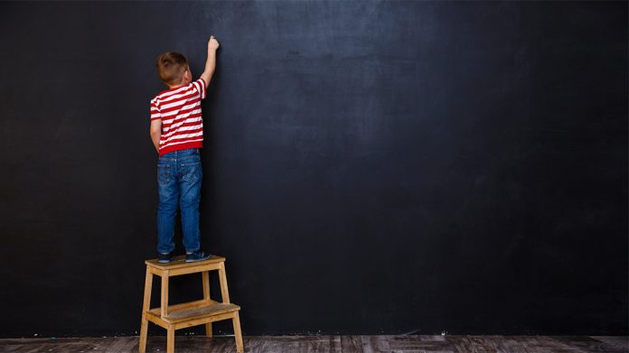 niño subido a una escalera escribiendo en una pizarra