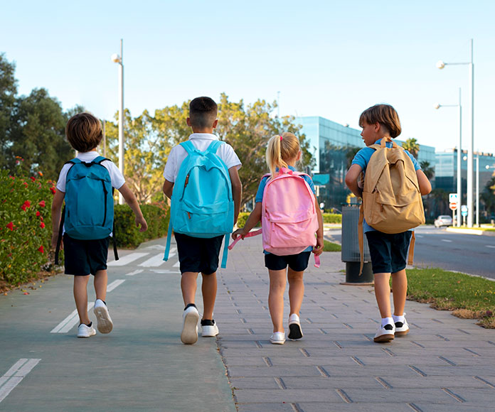 Niños caminando hacia la escuela con mochilas de colegio