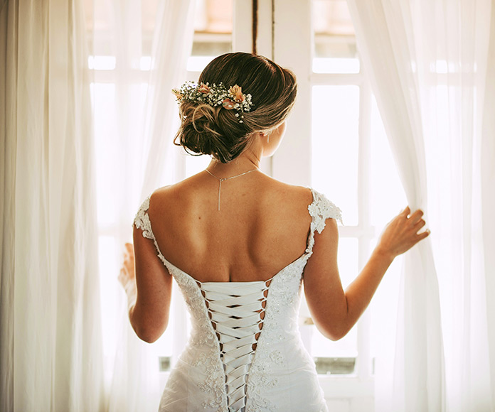 Mujer con vestido y peinado de novia mirando por la ventana